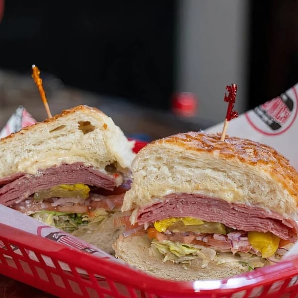 Two halves of a deli sandwich with meat, cheese, and vegetables in a red basket.
