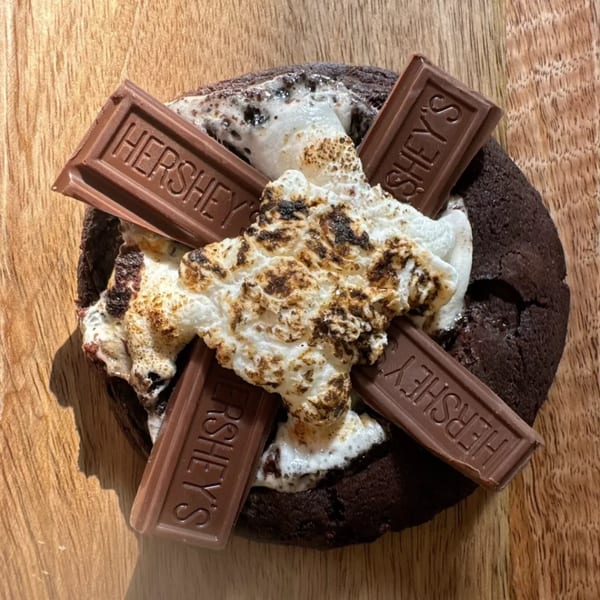 S'mores cookie with toasted marshmallow and Hershey's chocolate bars on a wooden surface.