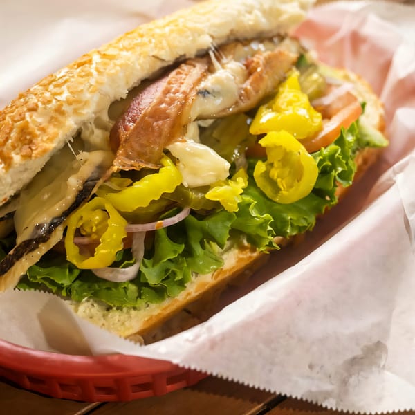 A close-up of a Sandwich Spot sandwich with bacon, cheese, lettuce, tomatoes, and peppers.