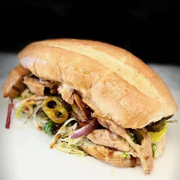 A large, appetizing sandwich from The Sandwich Spot, filled with meat, lettuce, onions, and peppers.